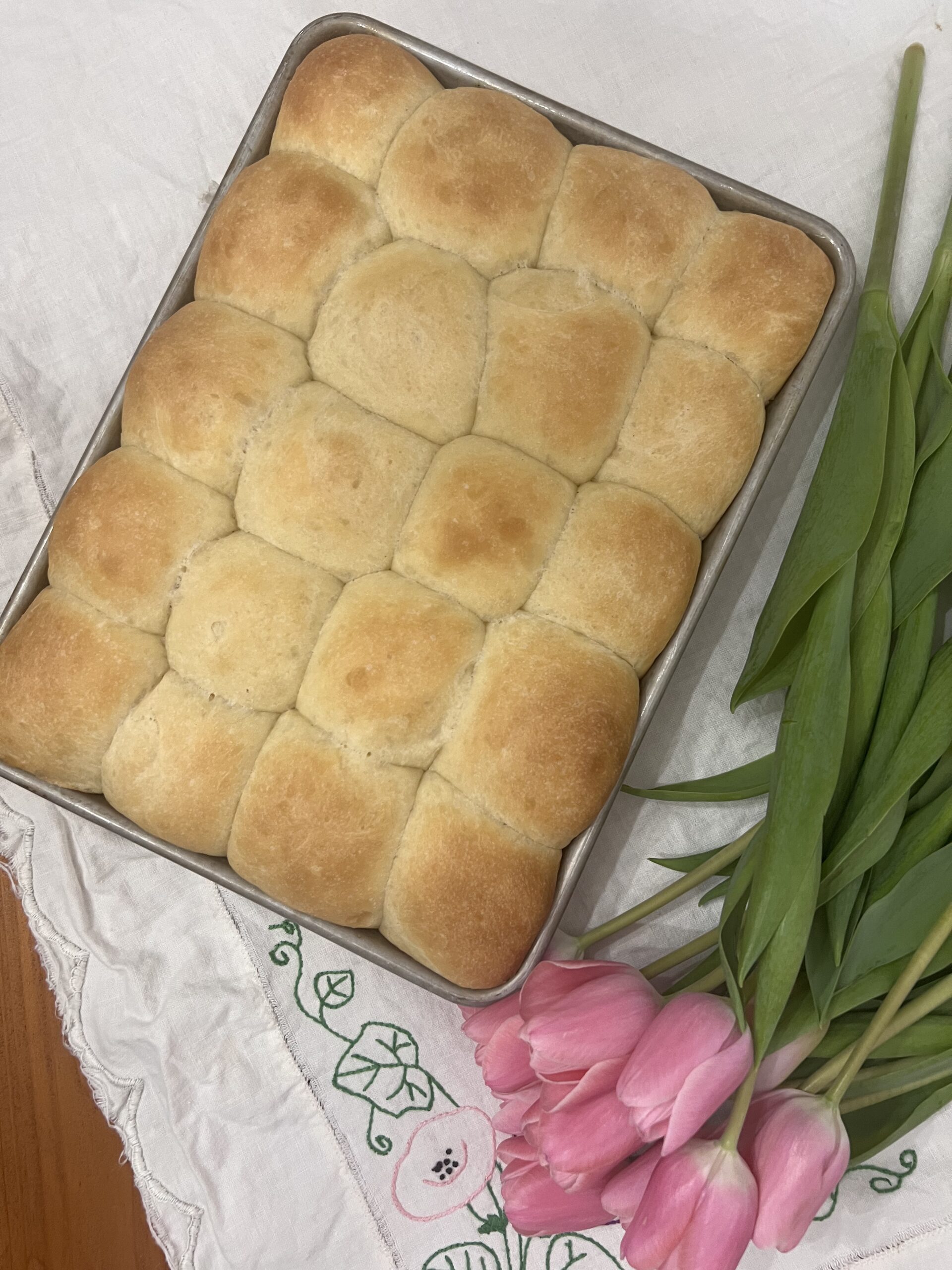 yeast rolls in metal pan on vintage embroidered table linen with pink tulips