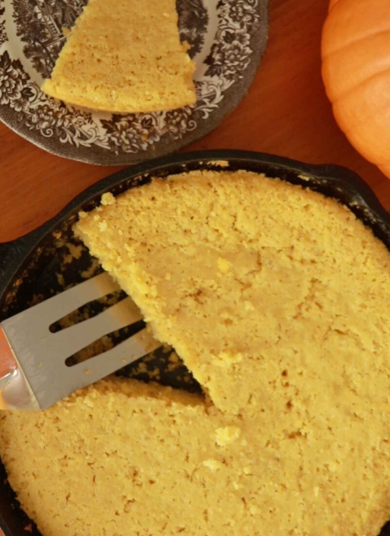 gluten free cornbread in a cast iron skillet with one slice pulled out on a vintage brown and white ironstone plate