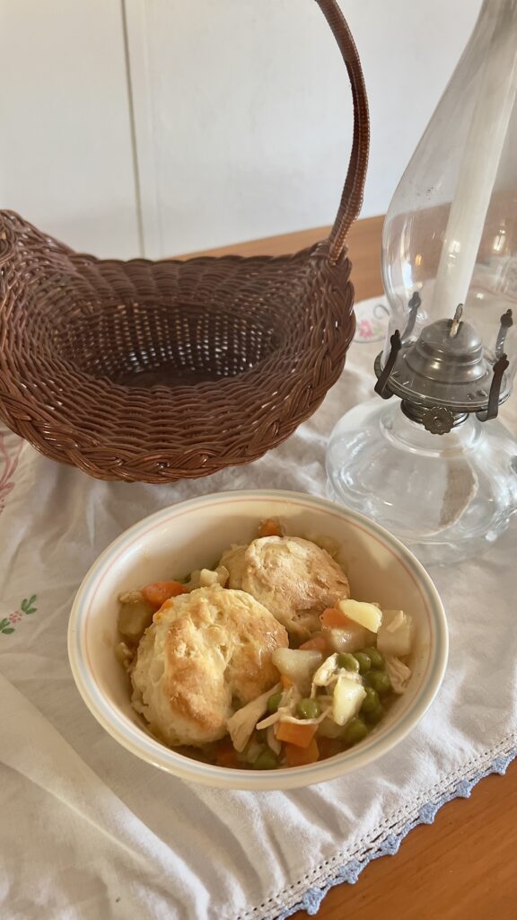 bowl of gluten free chicken pot pie with a gluten free biscuit topping on vintage tablecloth with a basket and antique oil lamp
