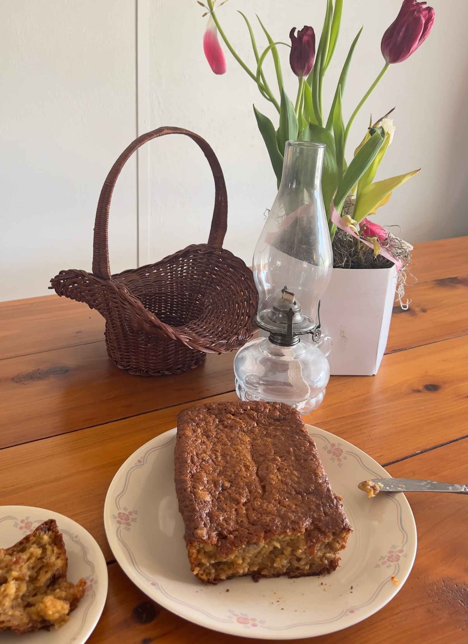 gluten free banana nut bread loaf that is sliced on a vintage correlle plate with vintage basket and oil lamp behind on a wooden table