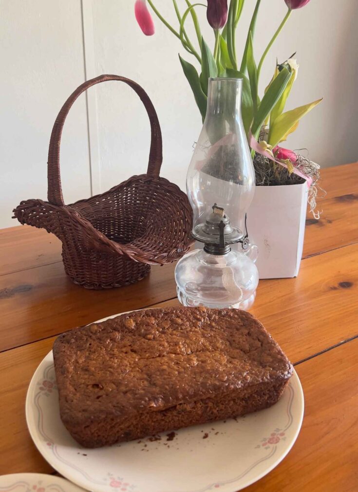 gluten free banana nut bread loaf on a vintage correlle plate with vintage basket and oil lamp behind on a wooden table