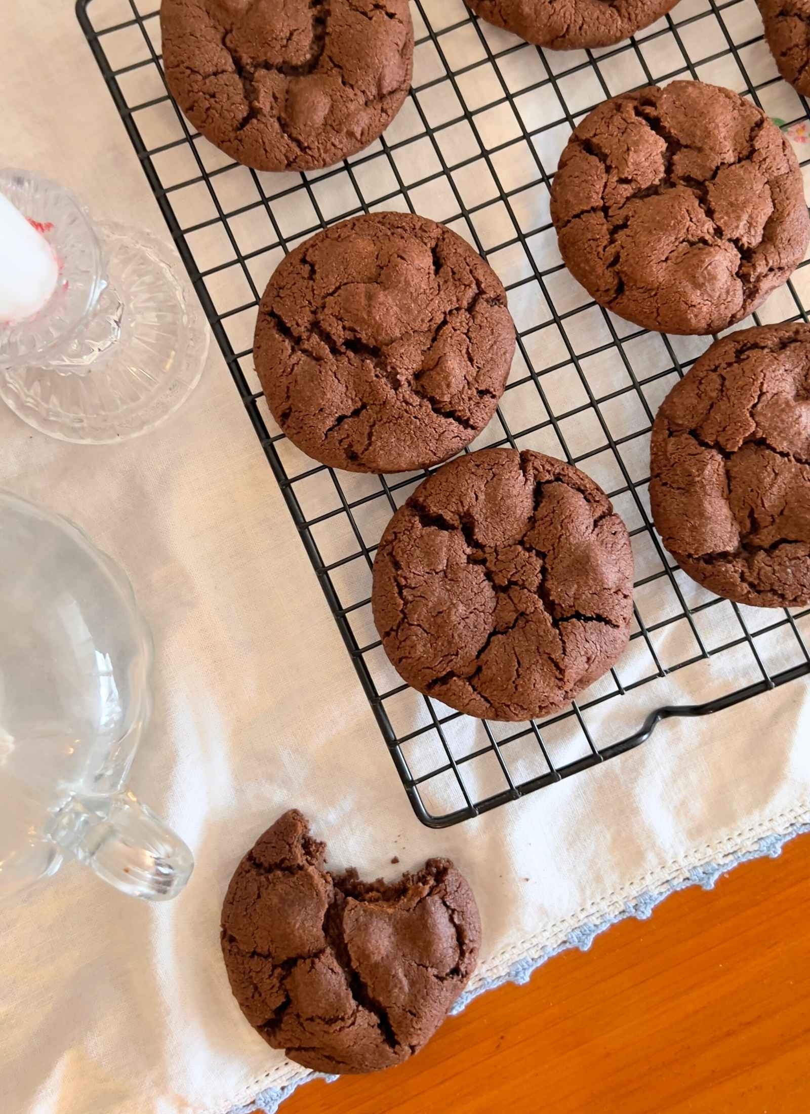 gluten free chocolate chocolate chip cookies on cooling rack with one cookie on vintage white tablecloth with bite taken out