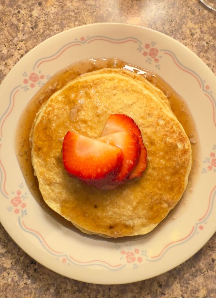 close up of gluten free oat flour pancakes with chopped strawberries and homemade syrup