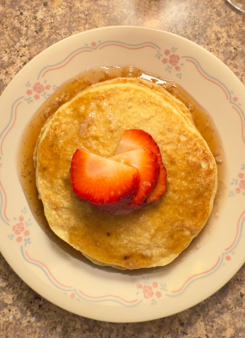 close up of gluten free oat flour pancakes with chopped strawberries and homemade syrup