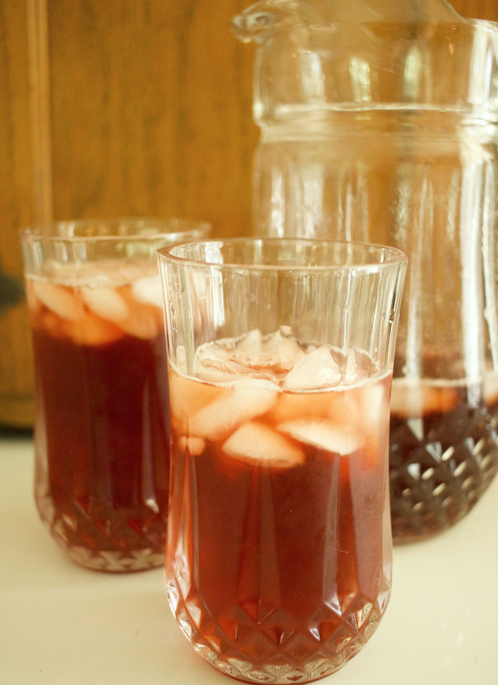 blackberry sweet tea in a vintage glass with ice cubes floating and a pitcher of tea behind