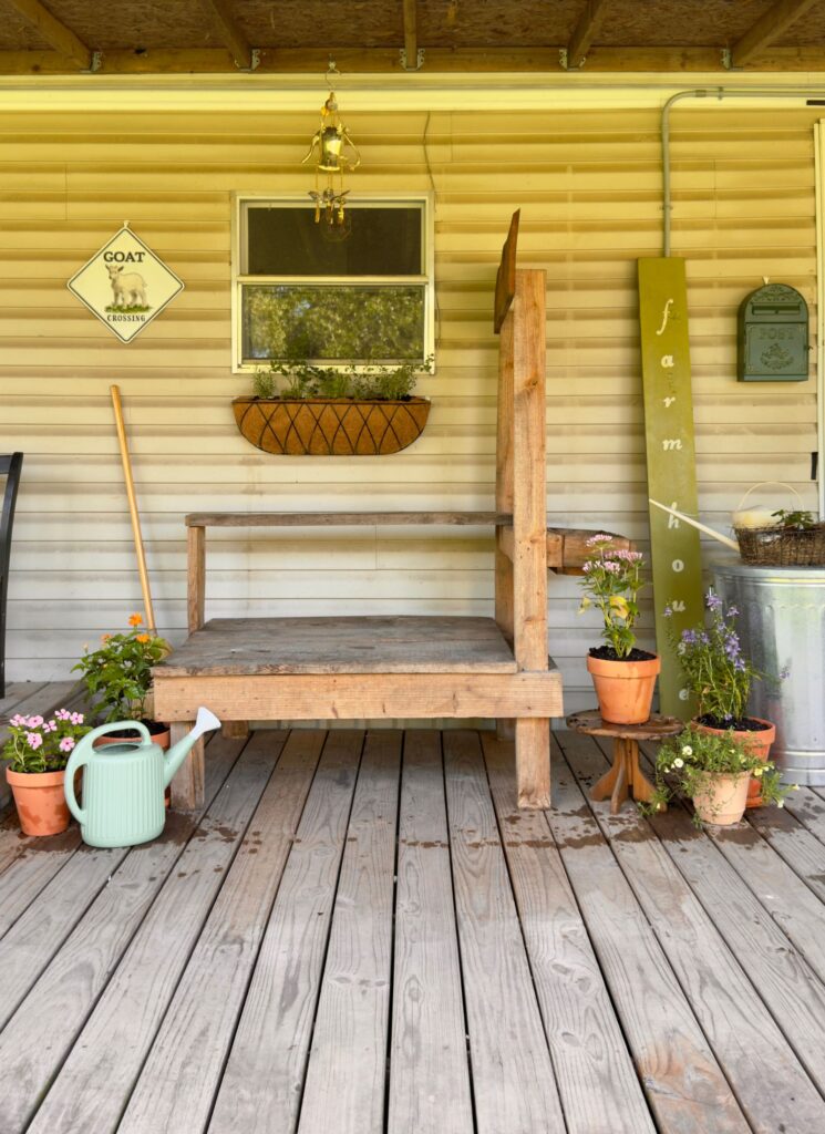 DIY Goat Milking Stand on the Farmhouse "milking" porch with potted flours and a few farmhouse signs
