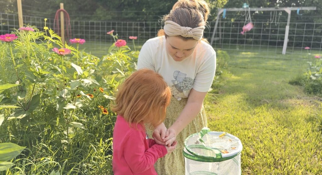 mom and daughter holding a butterfly to release in in the garden with zinnias behind