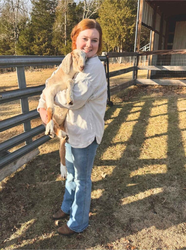 Girl holding a 4 week old nubian buckling in front of a metal gate