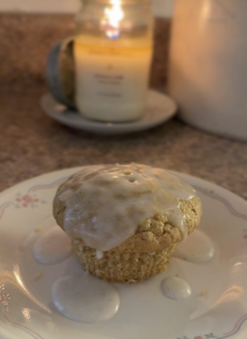 old fashioned donut muffin with glaze on a vintage correlle plate with a lit antique candle co candle in the background