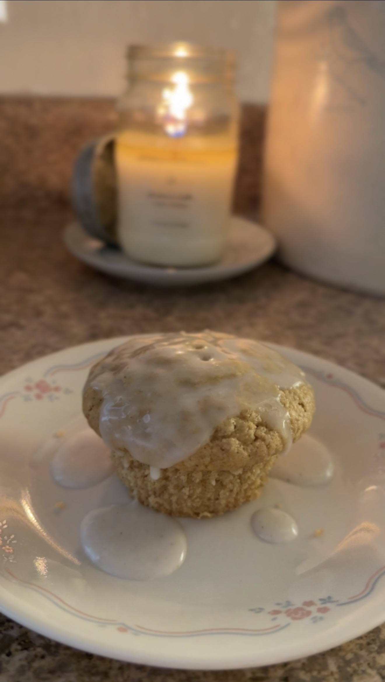 old fashioned donut muffin with glaze on a vintage correlle plate with a lit antique candle co candle in the background
