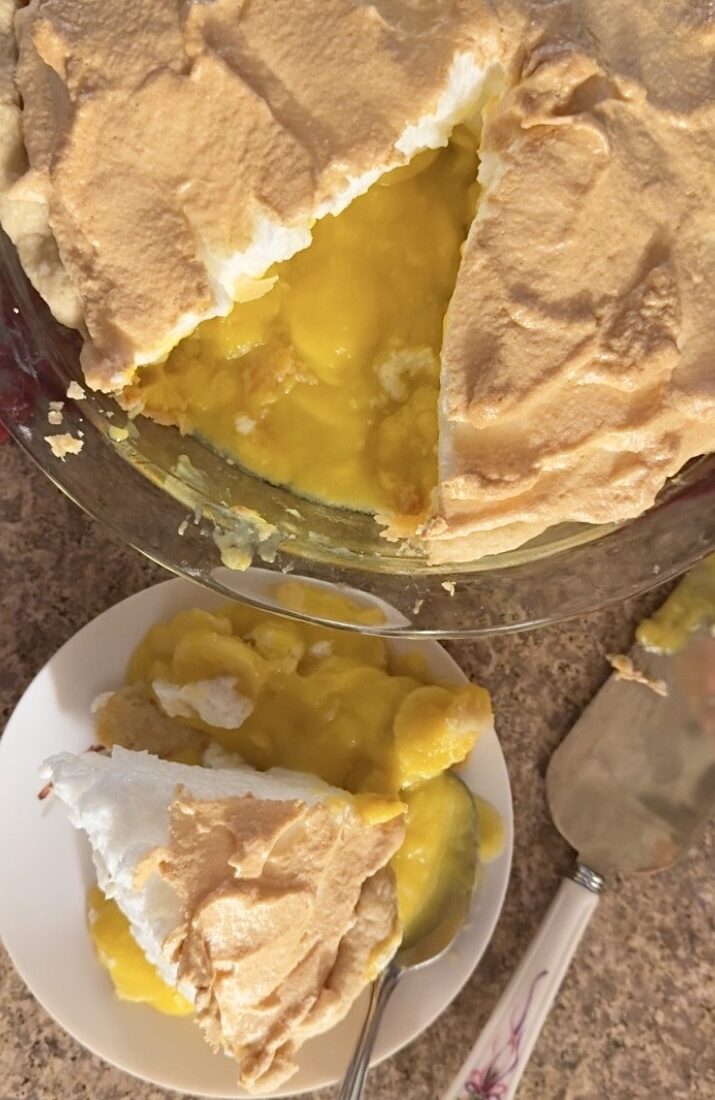 A banana cream pie sliced on a plate next to the pan of banana cream pie