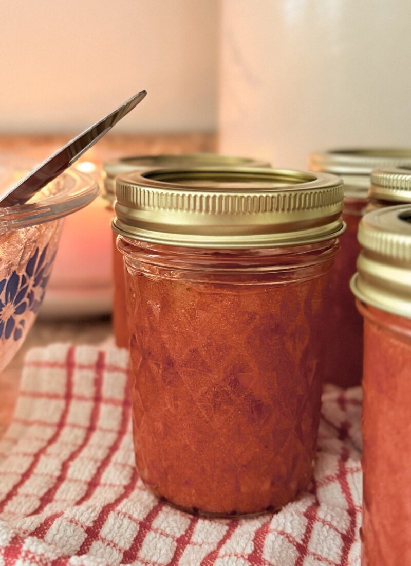 jar of strawberry freezer jam with gold lid sitting on vintage red and white checkered towel