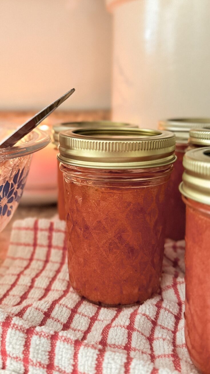 jar of strawberry freezer jam with gold lid sitting on vintage red and white checkered towel