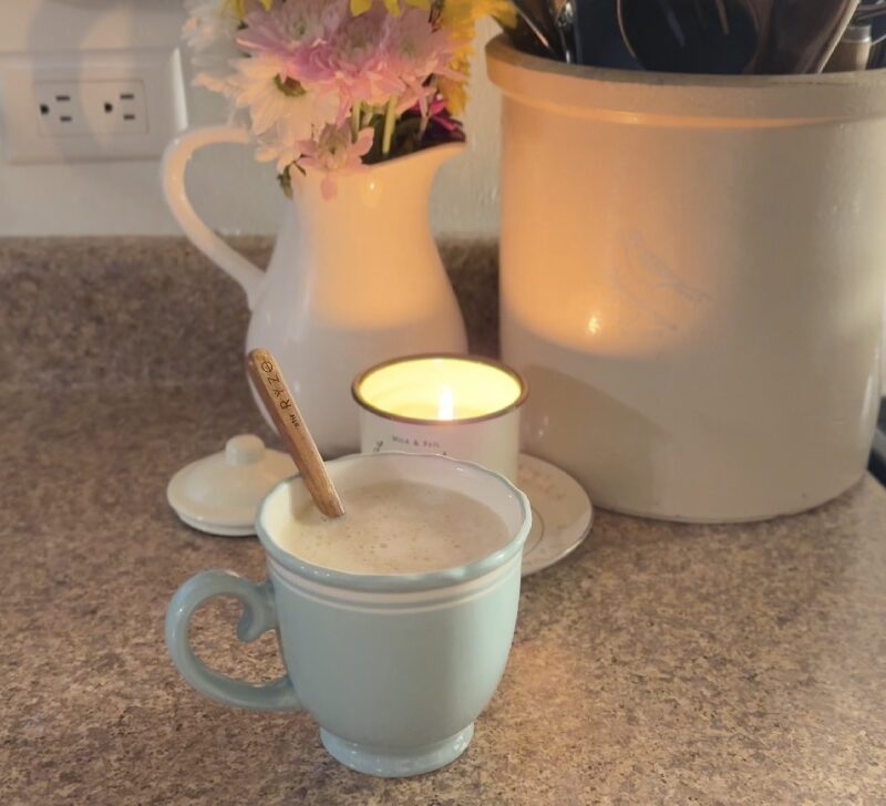 Sweet Cream and Honey Latte in a light blue mug with flowers and a lit candle behind