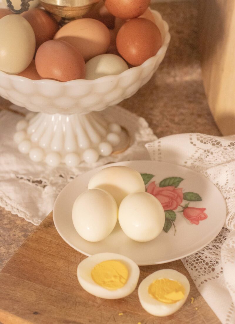 hard boiled eggs sitting on a rose melamine plate with a sliced hard boiled egg laid out in front on a wood cutting board.