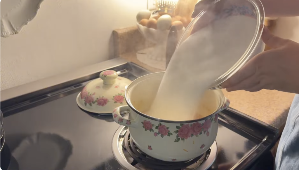 Pouring sugar into hot pot of orange marmalade mixture