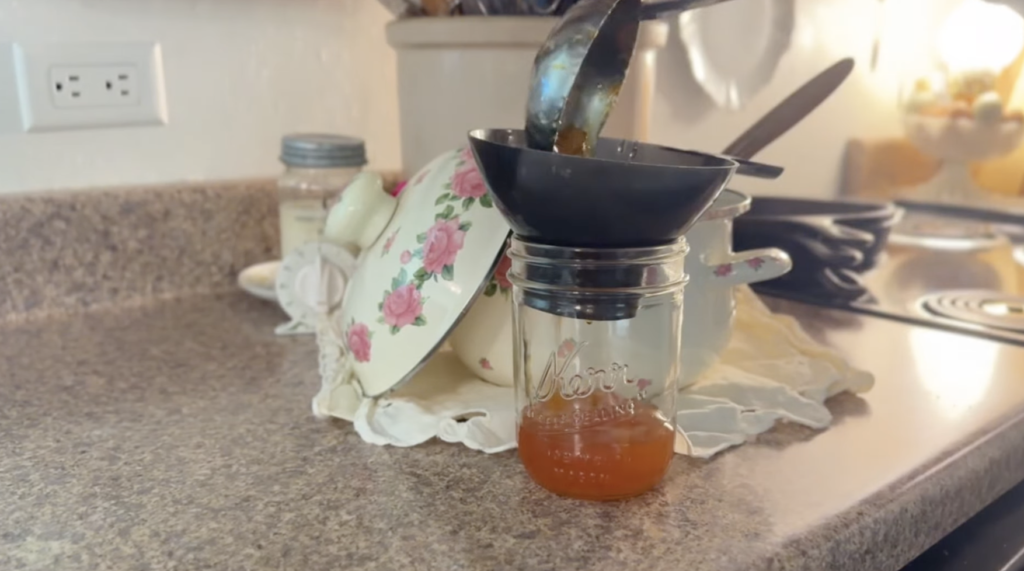 Ladling hot marmalade into pint size jars with a funnel. The jar is just a quarter full.