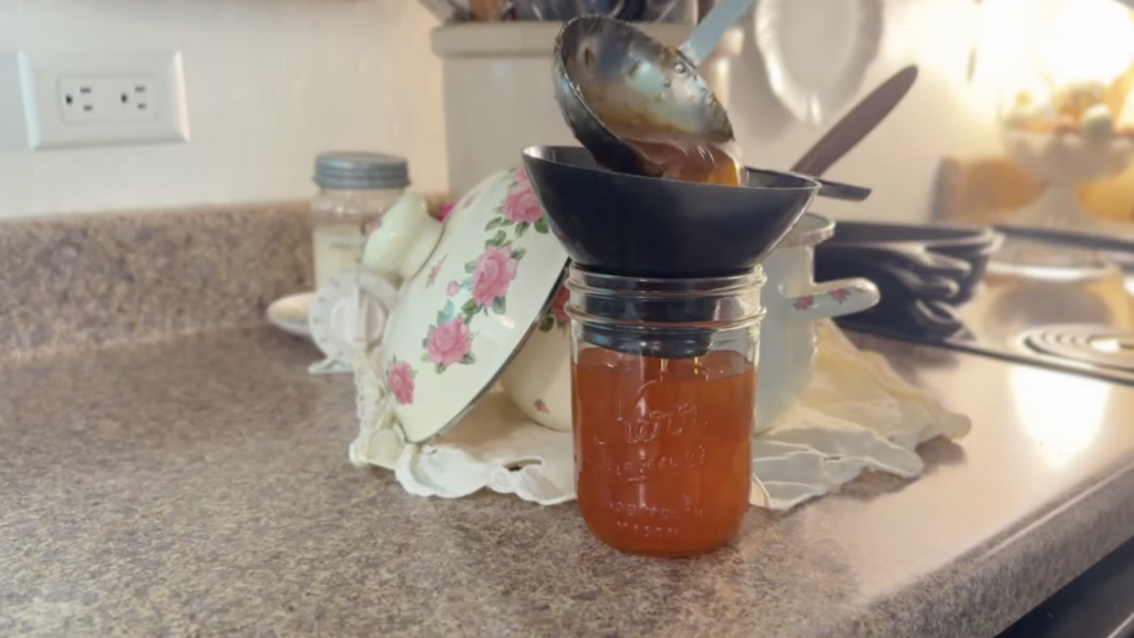 Ladling hot marmalade into pint size jars with a funnel. The jar is almost full.