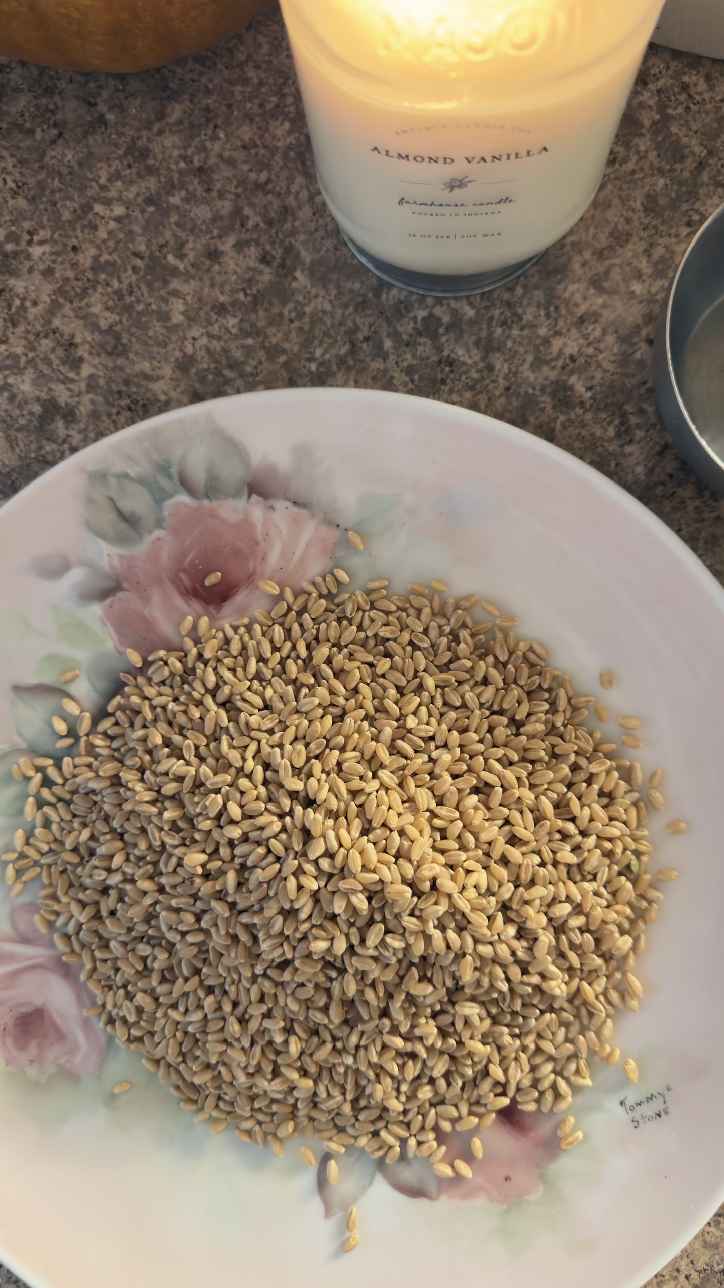 Wheat berries on vintage rose plate next to candle and measuring cup.