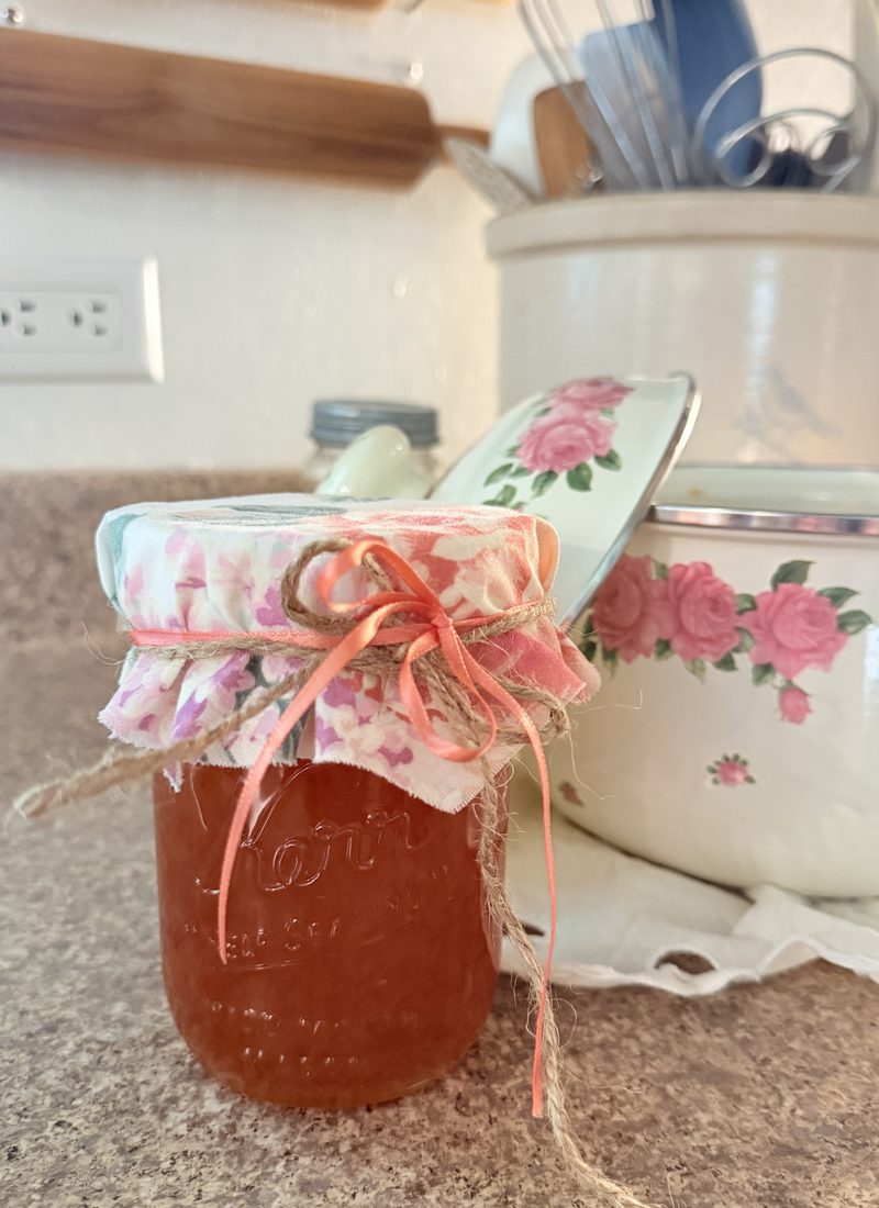 A pint jar of homemade orange marmalade sitting nice and pretty with a floral fabric jar topper and peach ribbon.