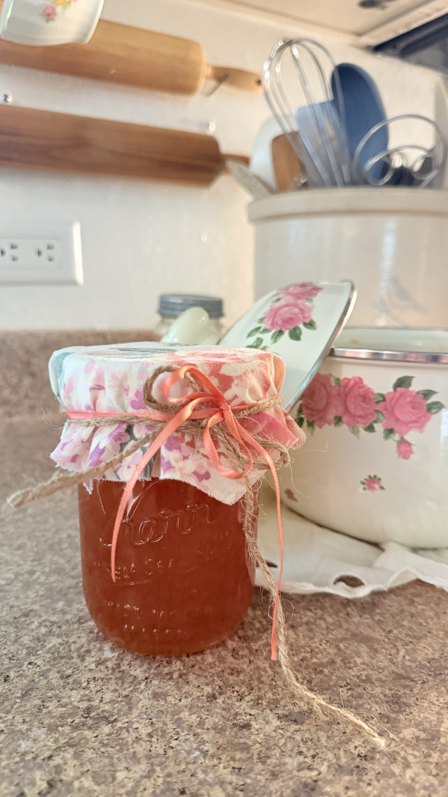 A pint jar of homemade orange marmalade sitting nice and pretty with a floral fabric jar topper and peach ribbon.